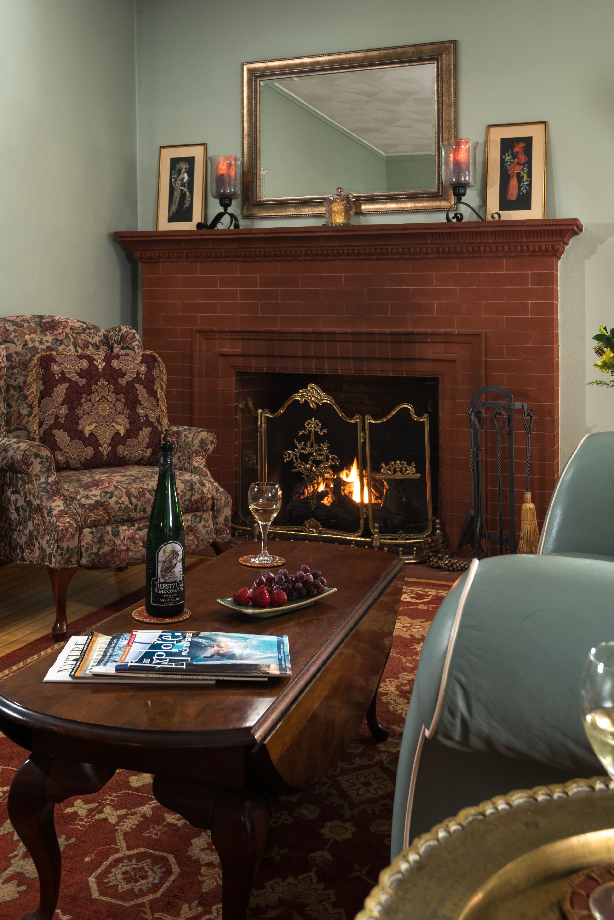 A living room with a fireplace, a sofa, a coffee table with magazines, and a bottle of wine.