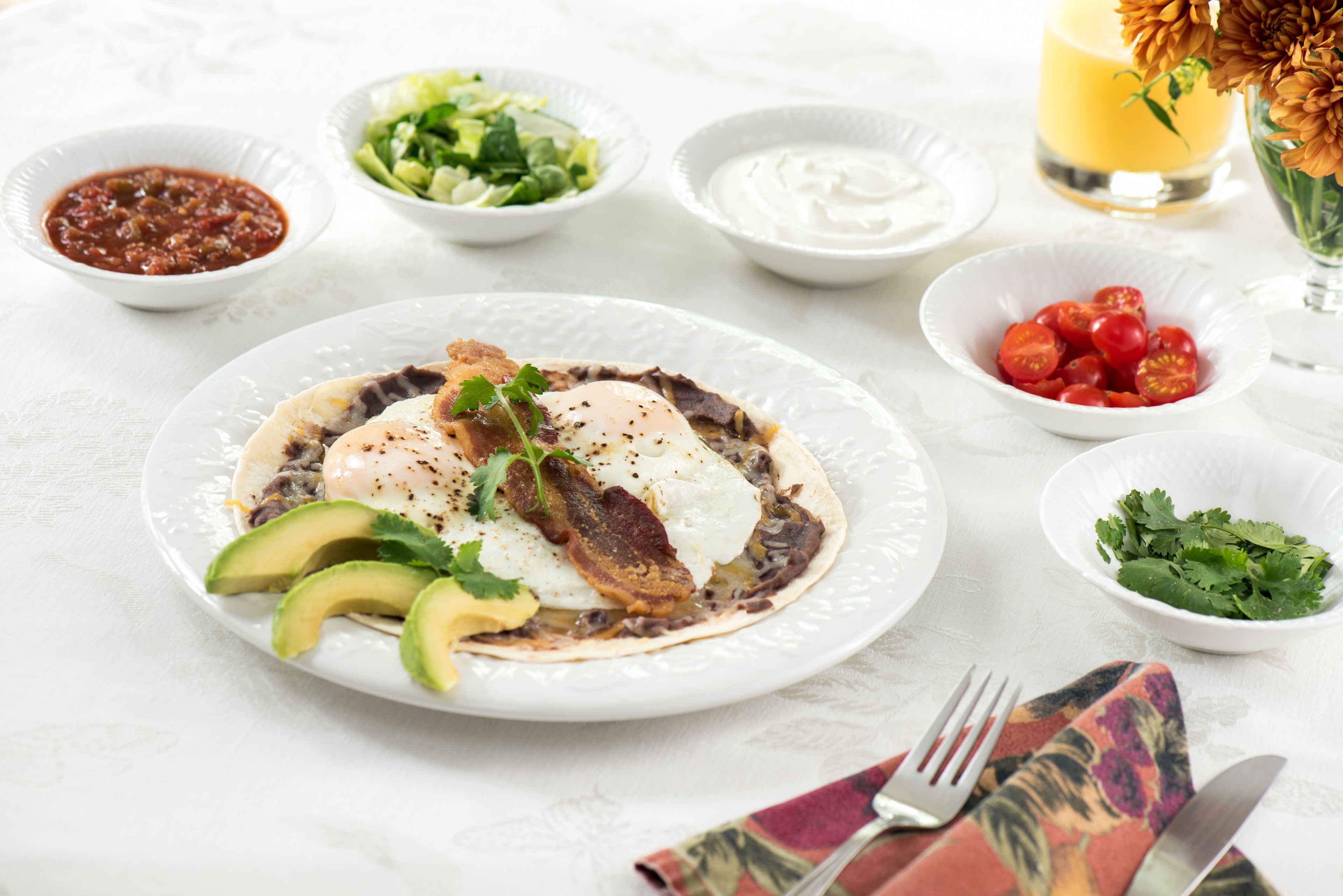 Un plato de desayuno con aguacate, huevos y tocino, rodeado de recipientes pequeños con salsas y una vela.