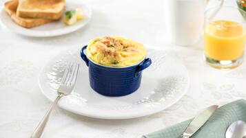 A breakfast setting with a blue ramekin containing a dish, a glass of orange juice, and toast on a white plate.