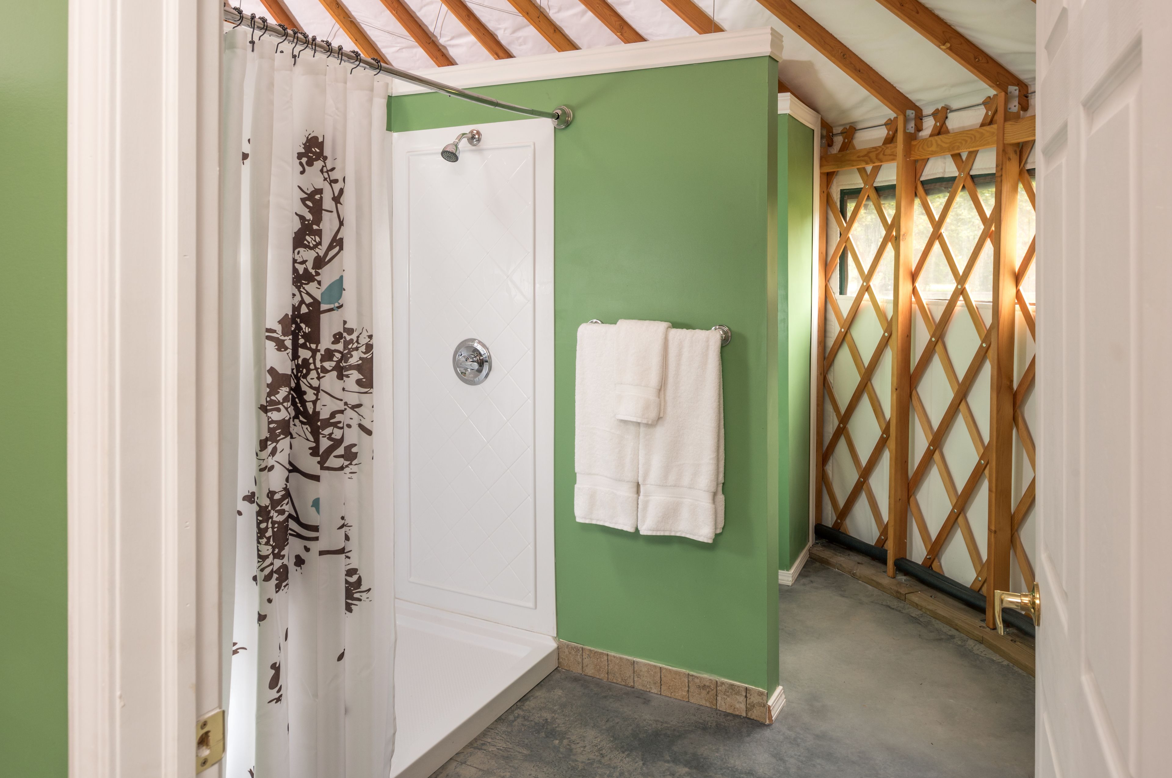 A bathroom with a shower, a towel rack, and a wooden lattice door.