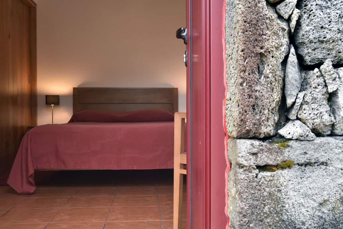 Une pièce avec un lit, une porte en bois et un mur en pierre.