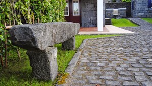 Un banco de piedra en un jardín con un sendero adoquinado que conduce a un edificio de piedra con una puerta roja.