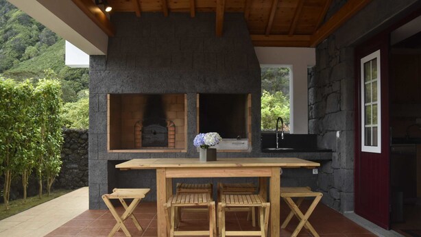 Una cocina al aire libre con pared de piedra, mesa de madera y dos sillas de madera.