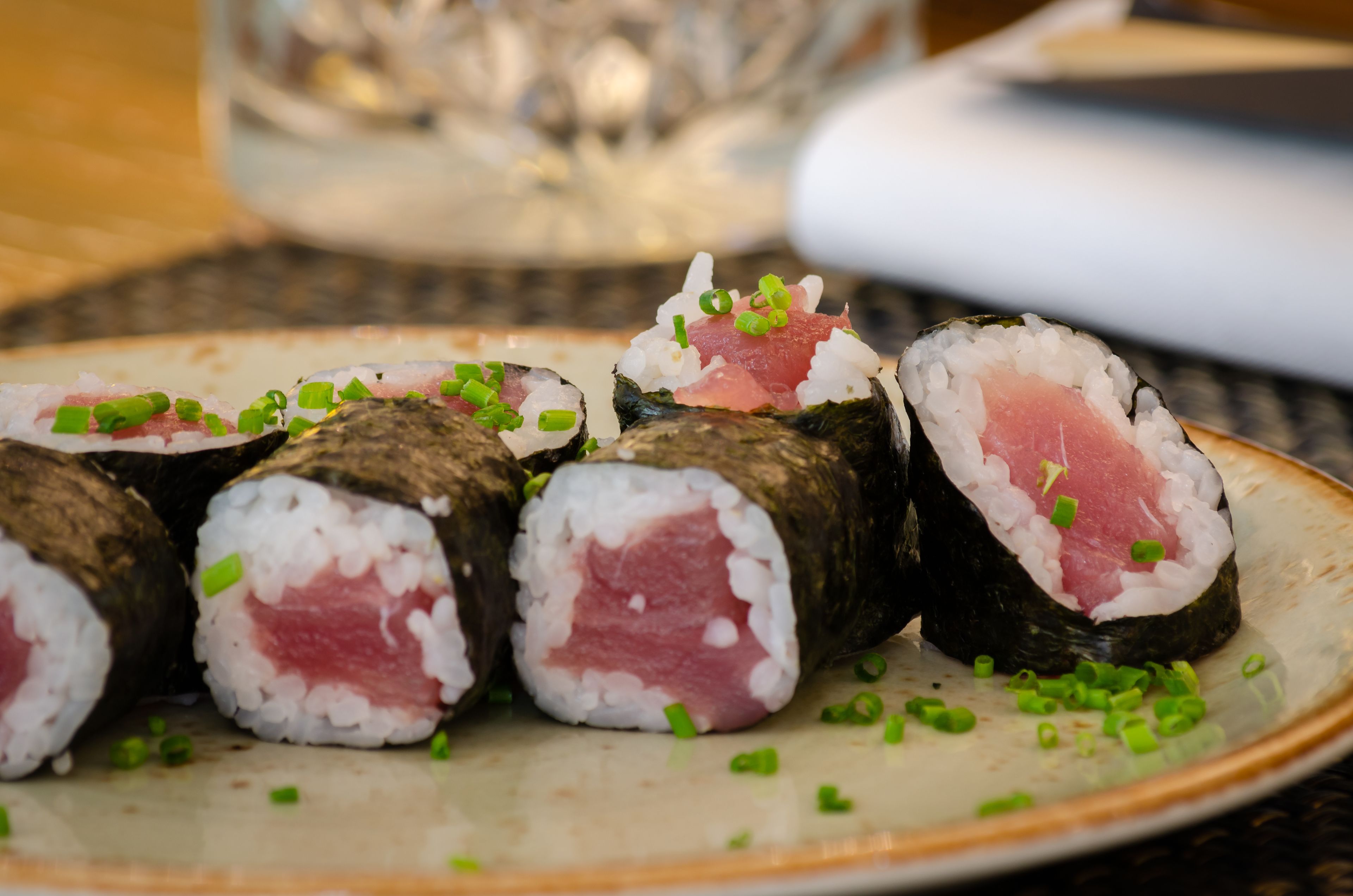 Des rouleaux de sushi préparés avec du riz blanc et du poisson rose, garnis d’oignons verts, présentés sur une assiette.