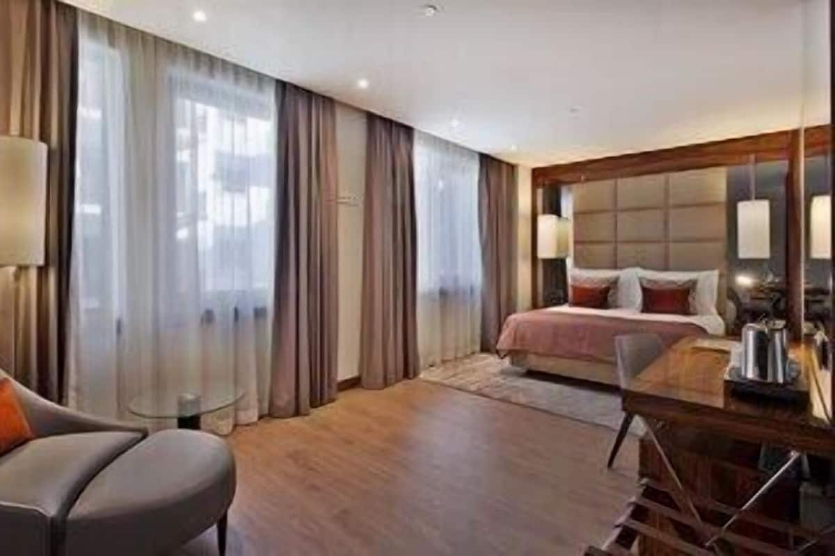 A hotel room with a bed, a desk, a chair, and a large window with curtains.