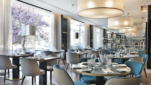 Un comedor moderno con mesas redondas, sillas azules y grandes lámparas colgantes.