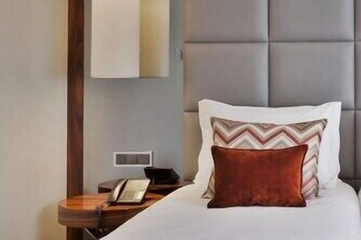 A hotel room with a bed, a bedside table with a phone, and a wall-mounted light fixture.