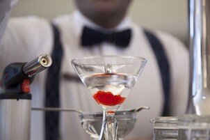 A martini glass with a red garnish, a cocktail shaker, and a bottle of water.