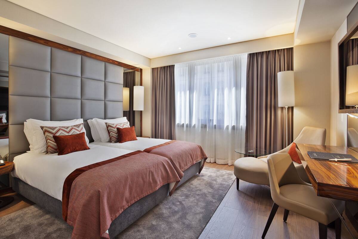 A modern hotel room with a large bed, a desk, and a chair.