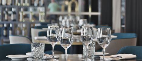 Un restaurante con mesas preparadas para comer, que presenta una moderna lámpara de araña y una estantería para vinos al fondo.