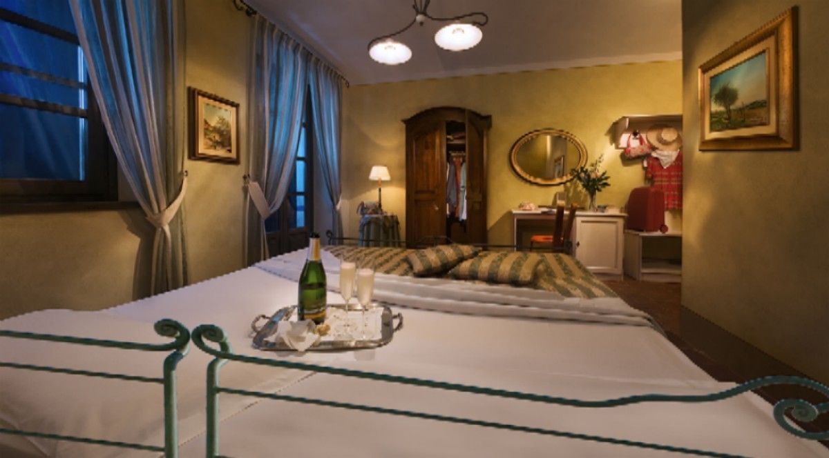 Una habitación de hotel con una cama, una mesita de noche con una botella y vasos, un espejo, un armario y un cuadro en la pared.