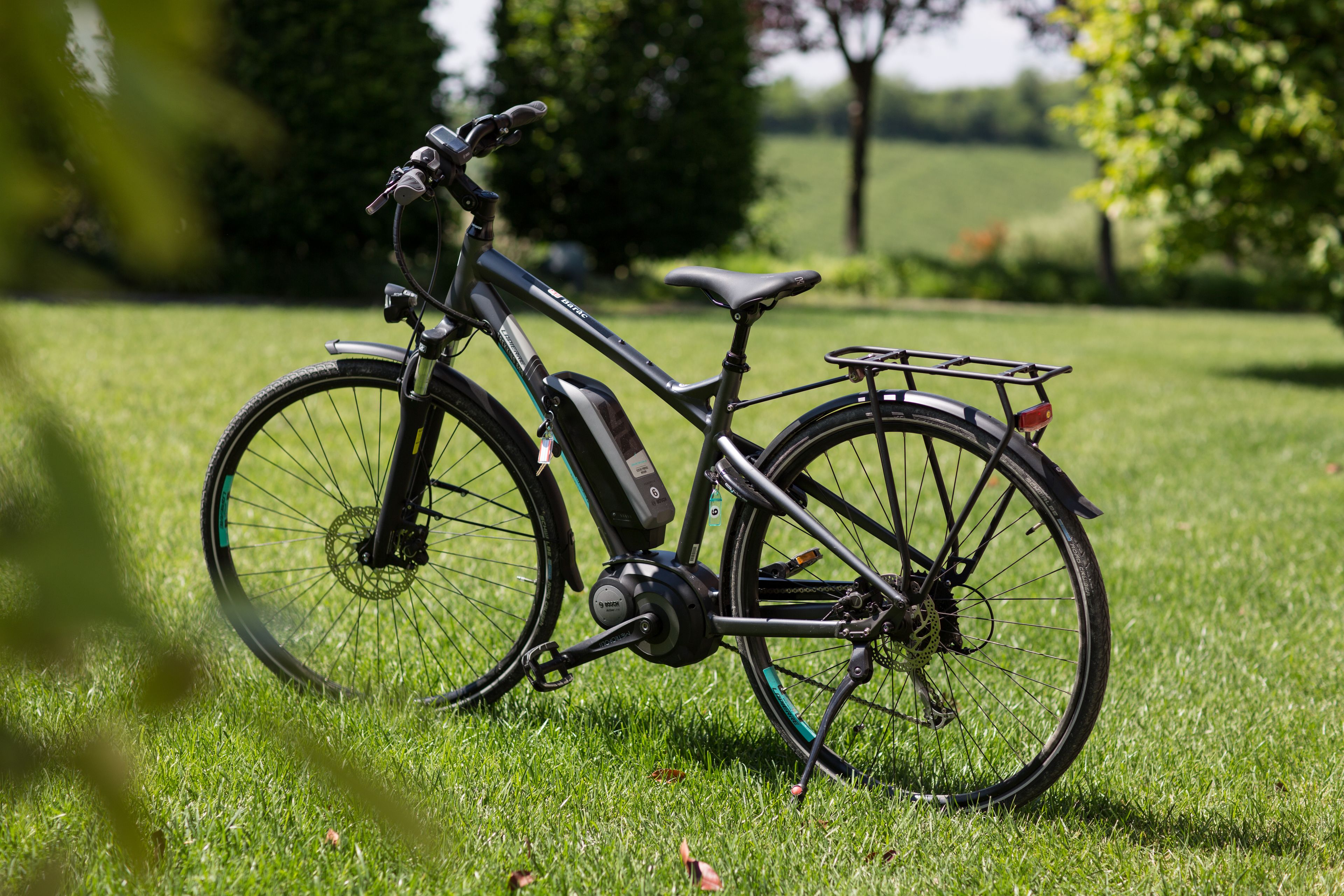 A stationary bicycle with a water bottle and a small rack on the rear, positioned on a grassy field with trees in the background.