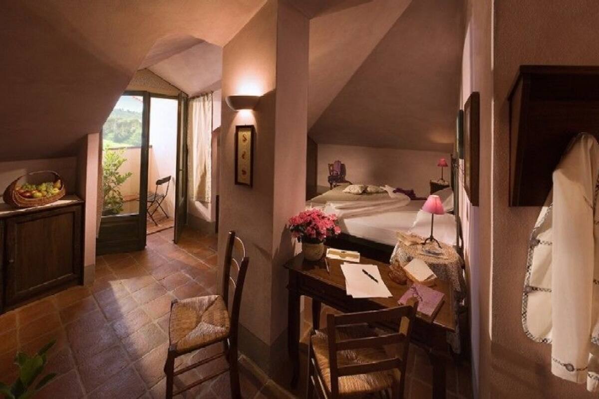 Un dormitorio acogedor con cama, escritorio y silla. Hay una ventana con cortinas, una planta y vistas al exterior.