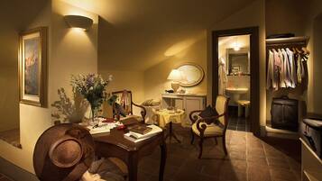 A warmly lit dining area with a wooden table, chairs, and a vase of flowers. A mirror and a lamp are on the wall.