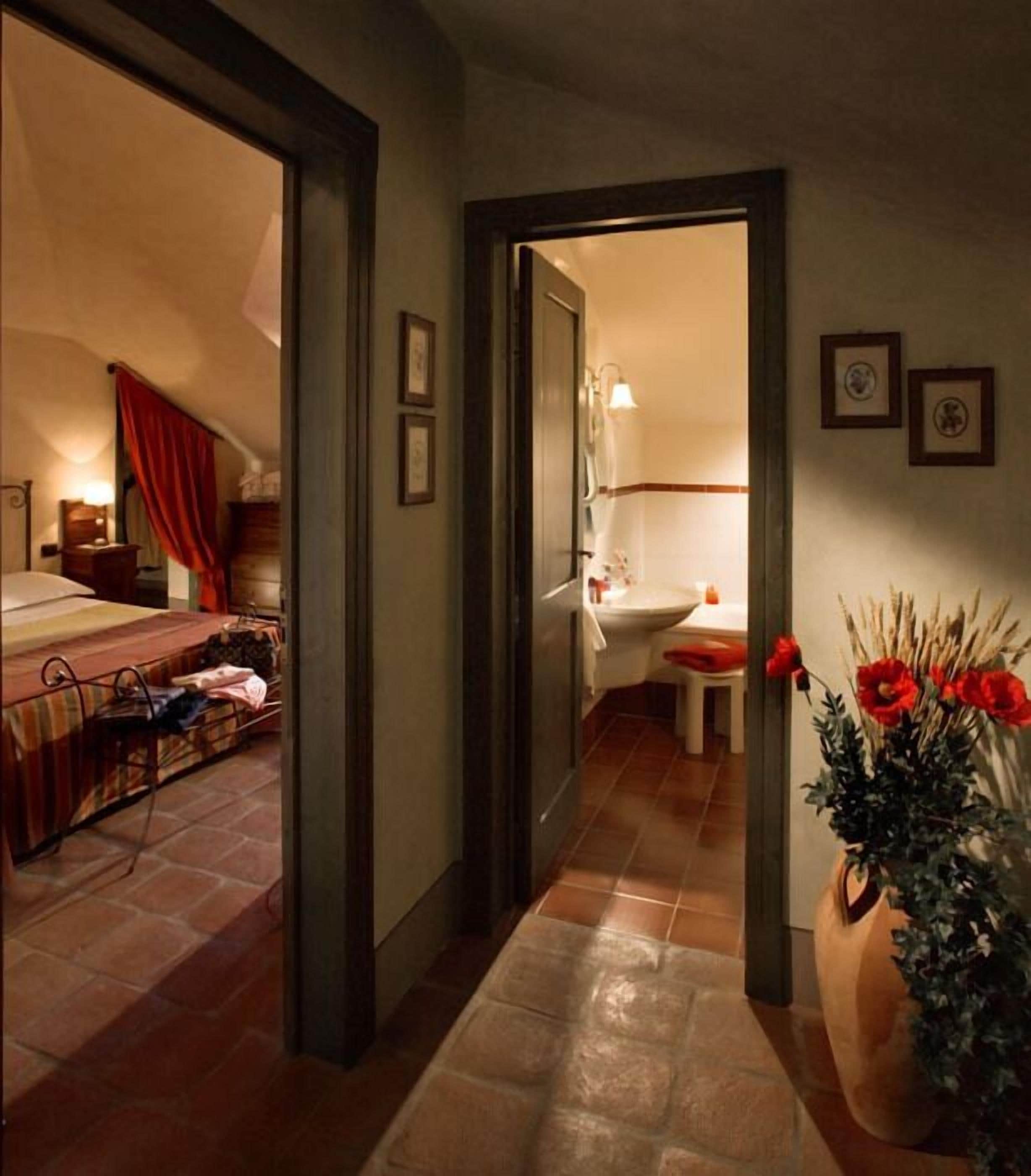 A hotel room with a bed, a nightstand, a desk, and a bathroom visible through an open door.
