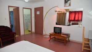 A hotel room with a bed, a TV on a wooden stand, a red chair, and a mirror with a red curtain. - Hôtel Résidence Les Anges (Lomé)
