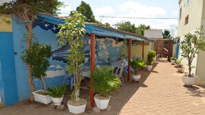 A courtyard with potted plants, a mural, and a tiled walkway. - Hôtel Résidence Les Anges (Lomé)
