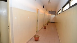 A narrow hallway with tiled flooring and white walls, featuring several potted plants and doors along the sides. - Hôtel Résidence Les Anges (Lomé)