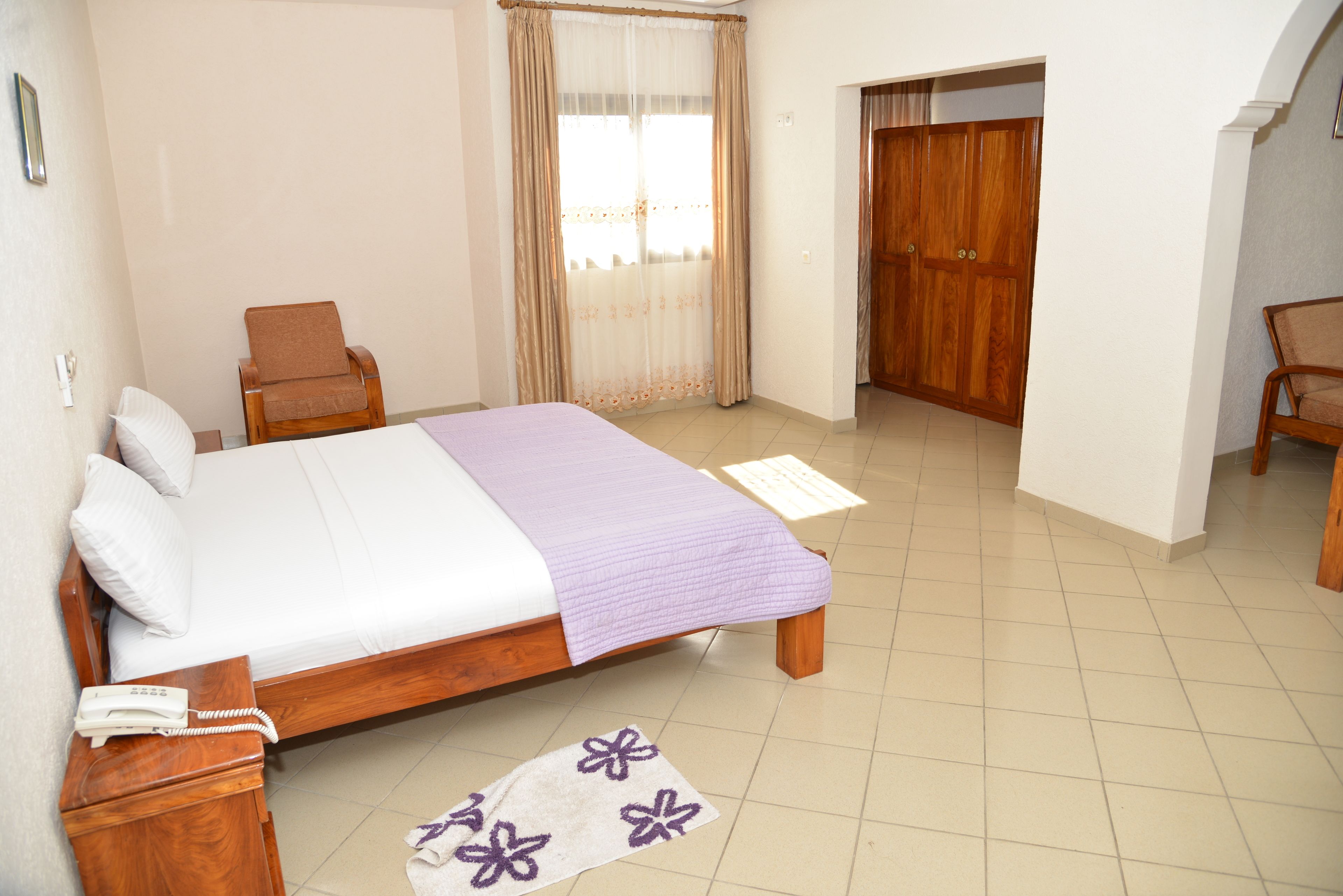 A bedroom with a bed, a chair, a wooden wardrobe, and a door leading to another room.