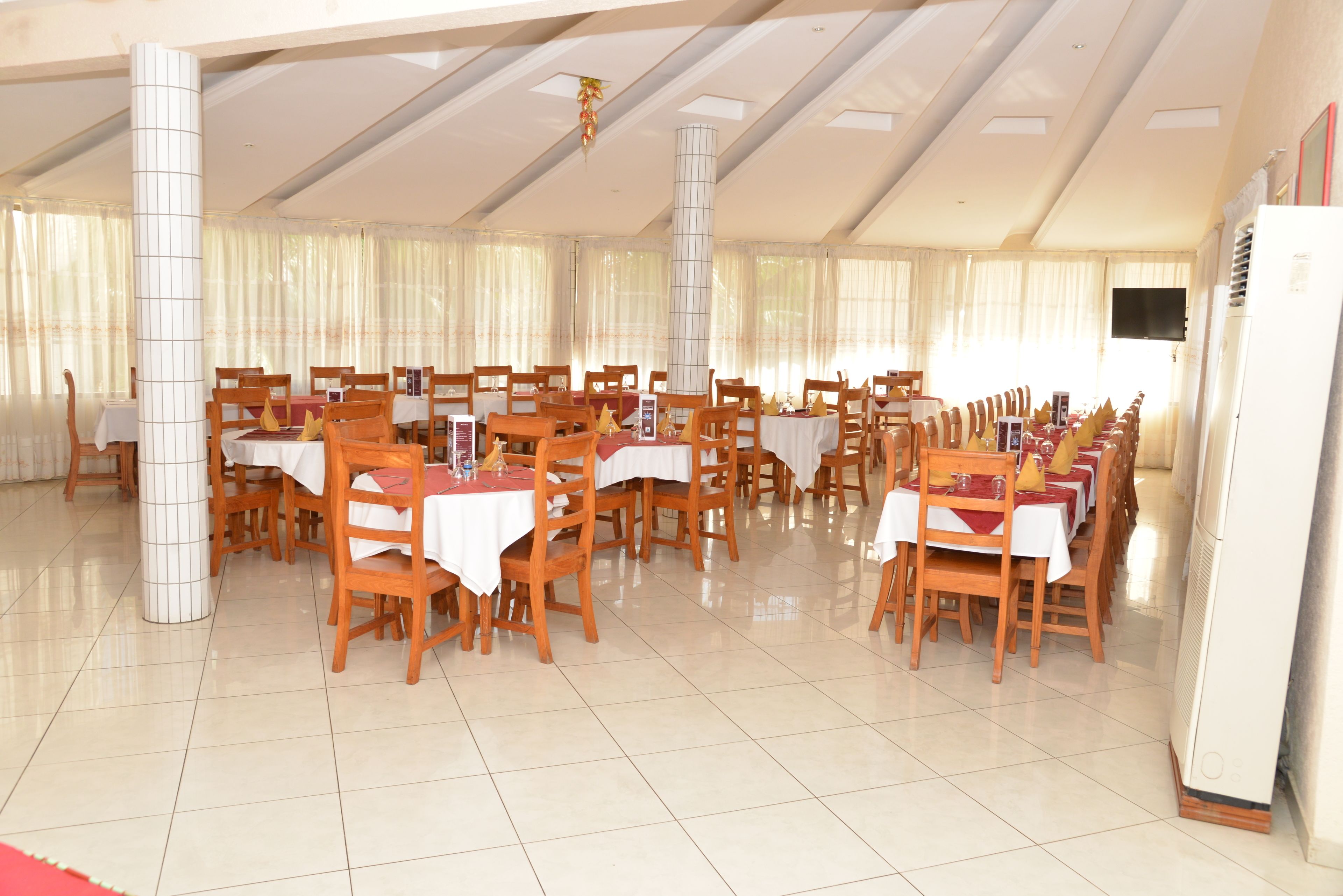 A spacious dining hall with multiple tables and chairs, large pillars, and a tiled floor.