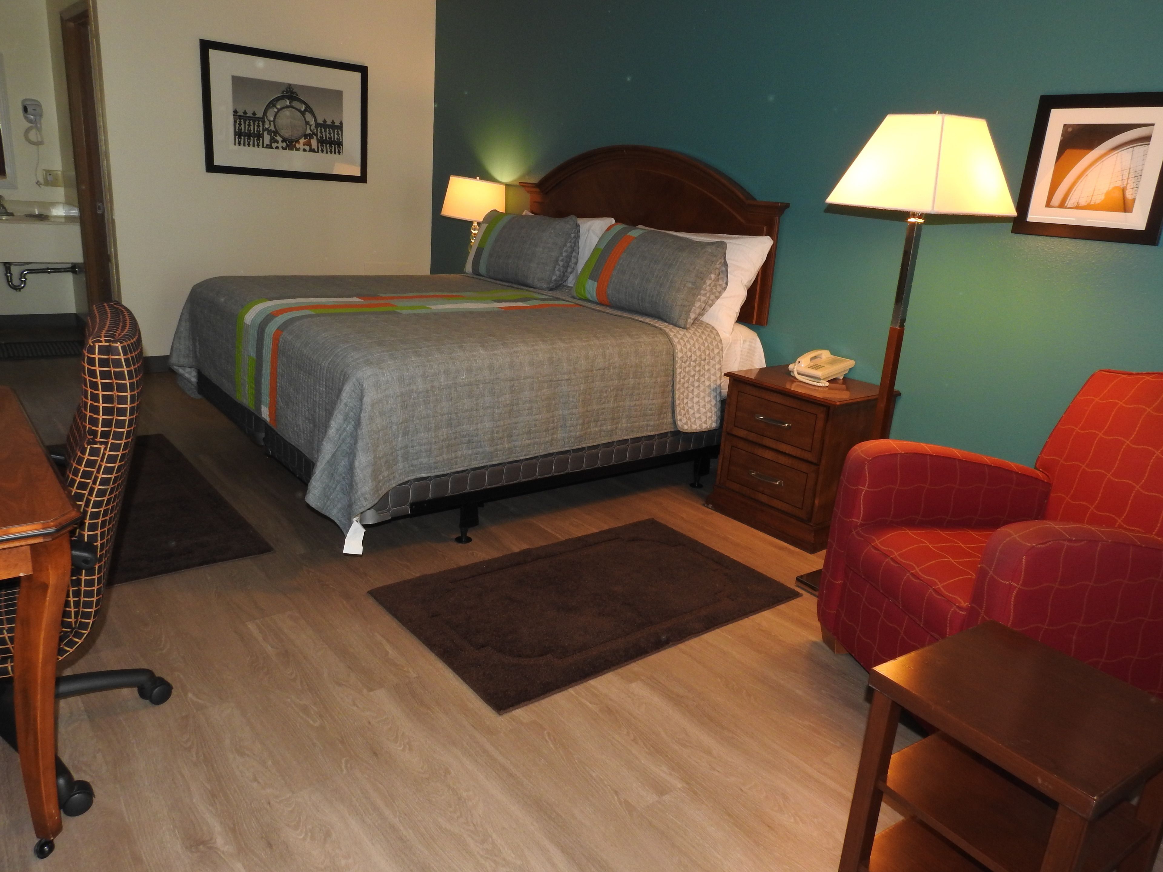 A neatly arranged hotel room with a bed, bedside tables, a desk, a chair, and a lamp.