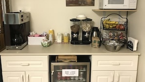Una kitchenette con cafetera, microondas y refrigerador. Hay varios alimentos y condimentos en la encimera.