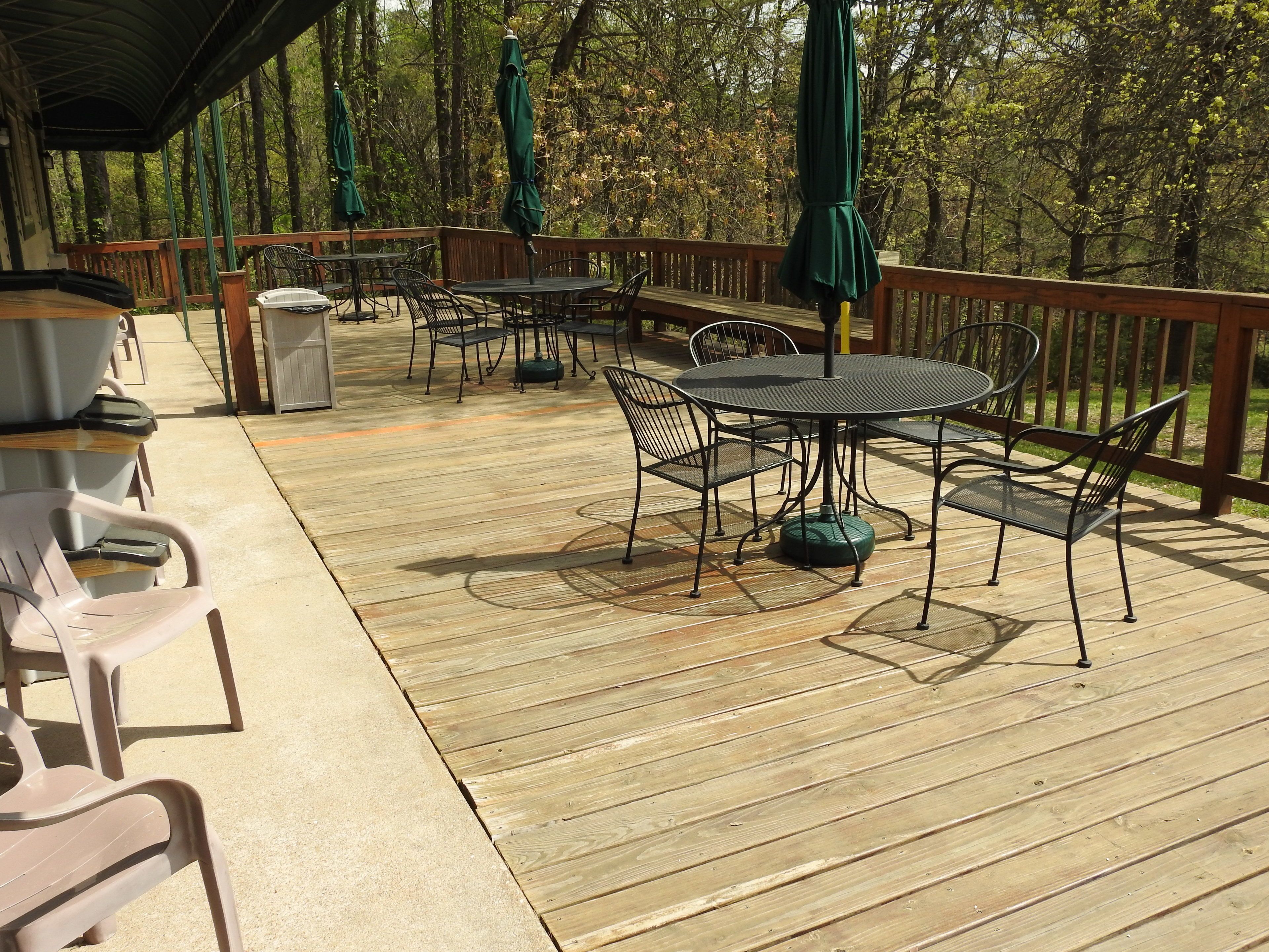 Une terrasse extérieure avec un plancher en bois, des tables et des chaises en métal, et des parasols verts.