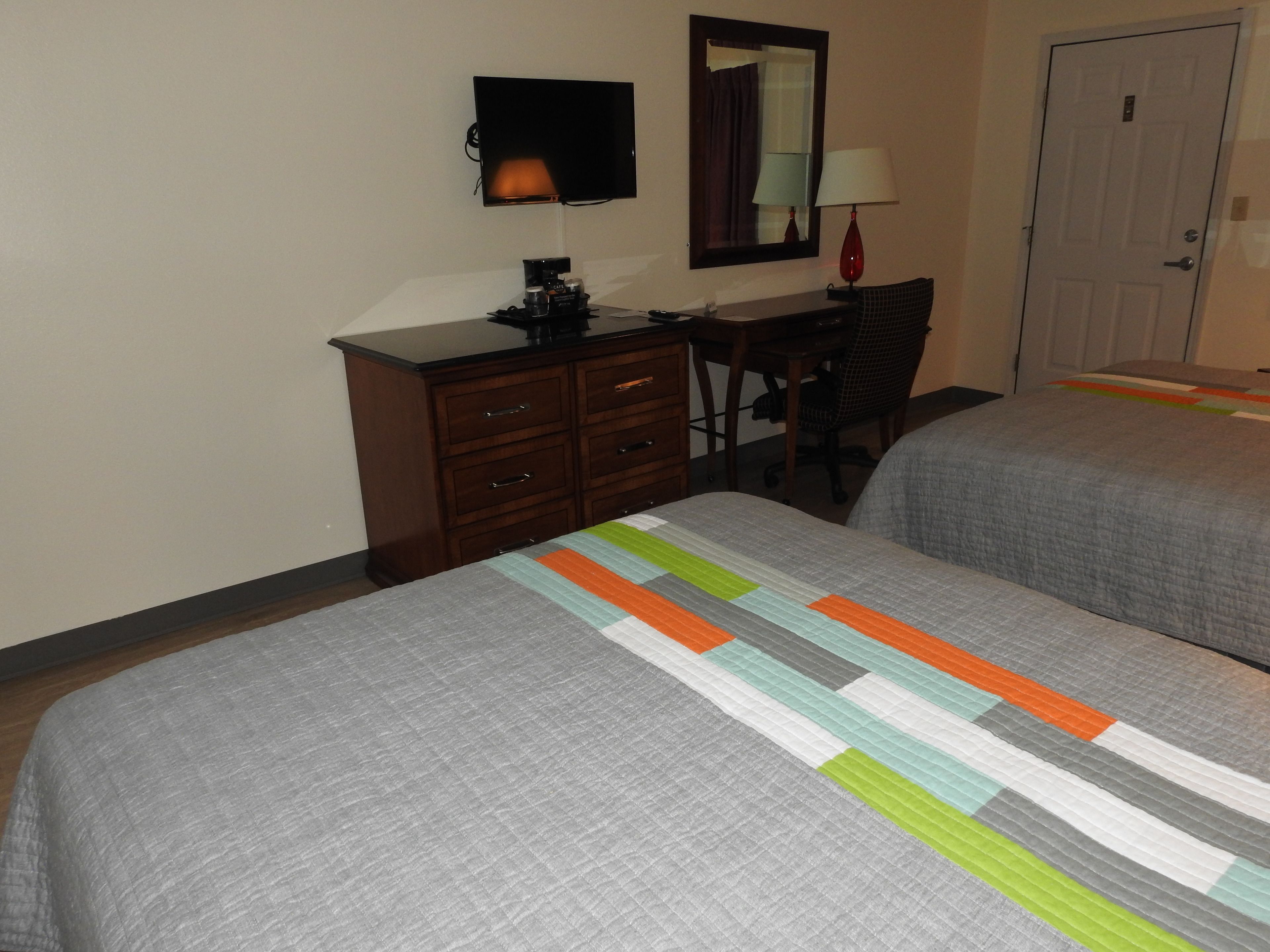 A hotel room with two beds, a desk with a chair, a dresser, a TV, and a door.