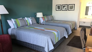 Una habitación de hotel con dos camas, un escritorio, una silla y una lámpara.