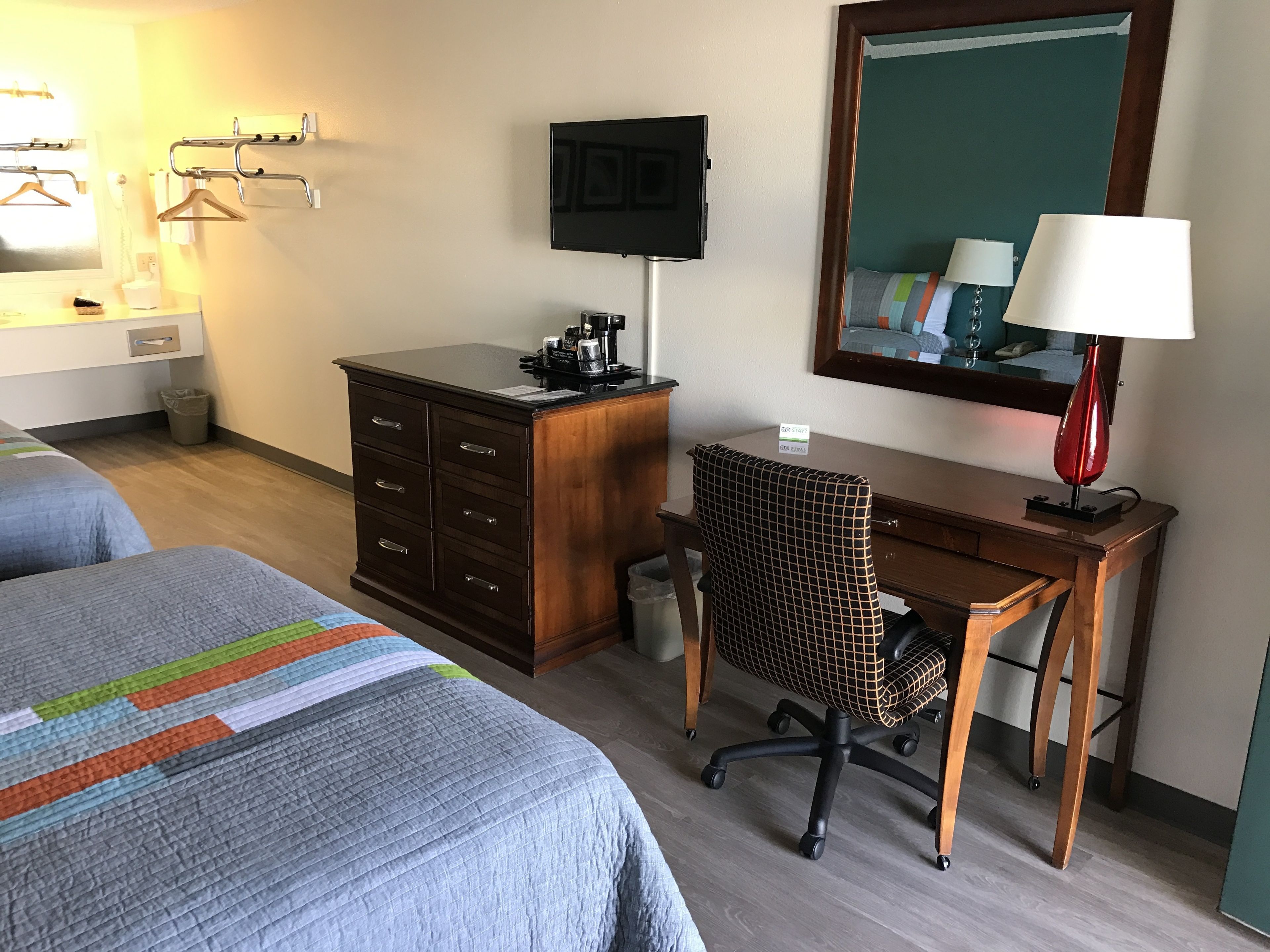 A hotel room with two beds, a desk with a chair, a TV, a lamp, and a mirror.