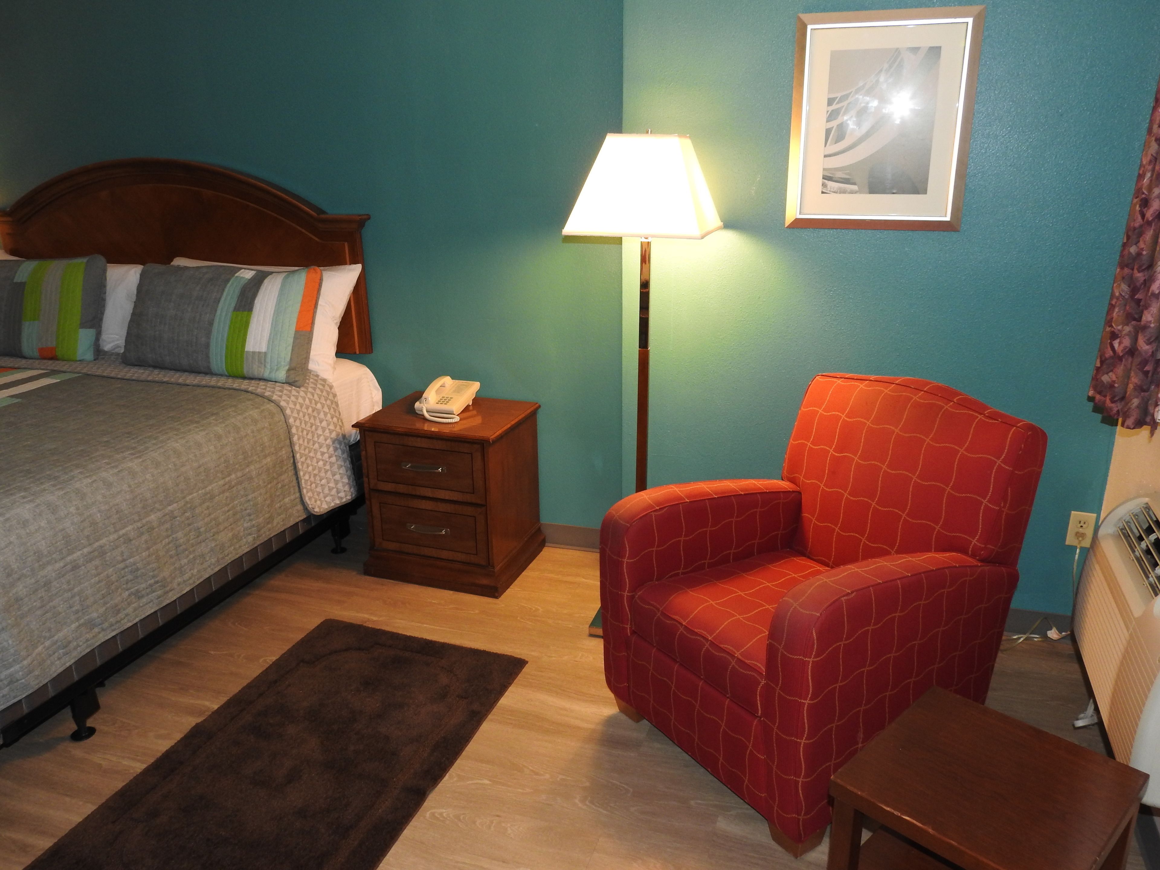Ein Hotelzimmer mit einem Bett, einem Nachttisch mit Lampe, einem roten Sessel und einem kleinen Tisch.