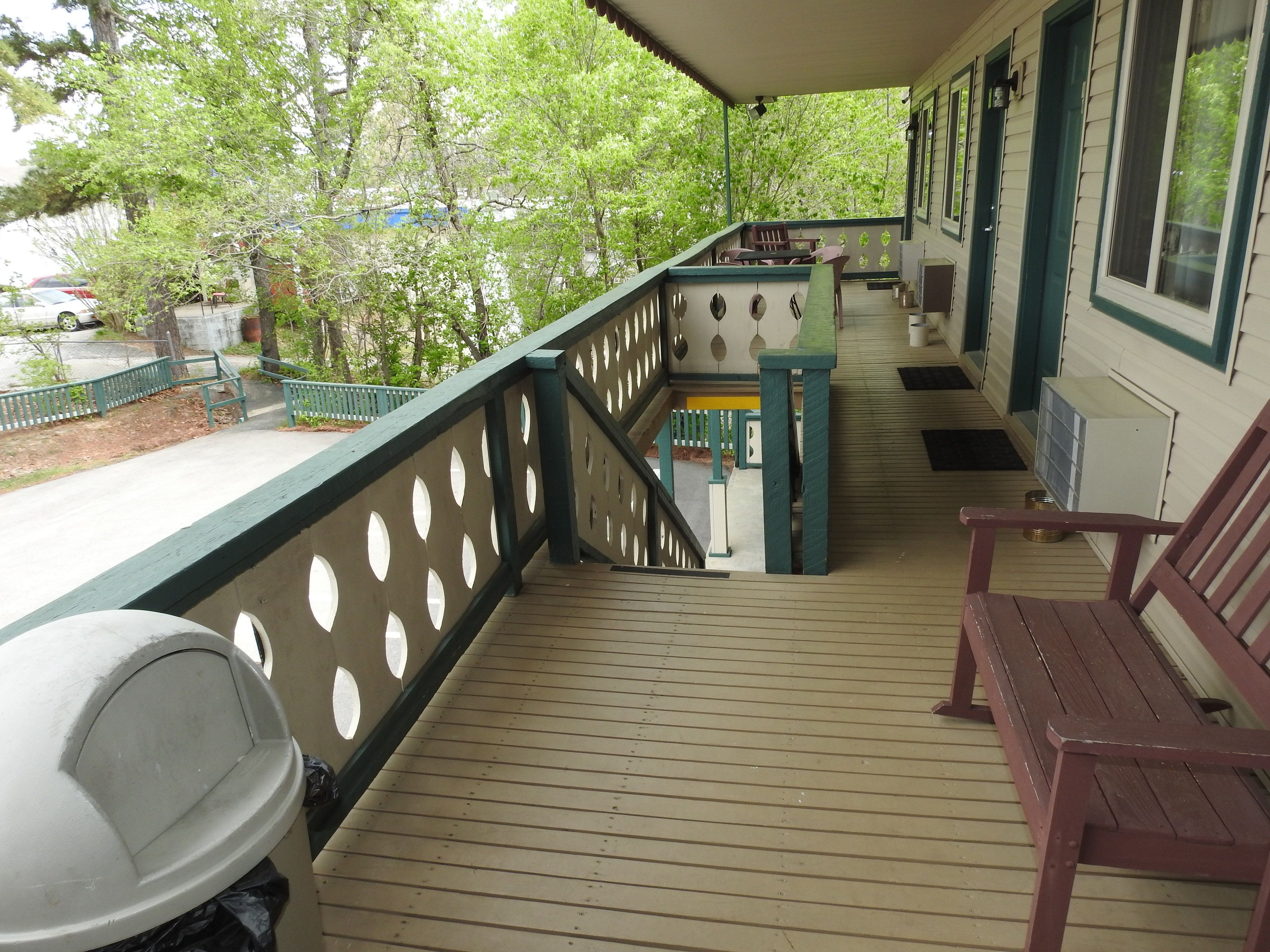 A covered porch with a wooden deck, a barbecue grill, and a seating area with chairs.