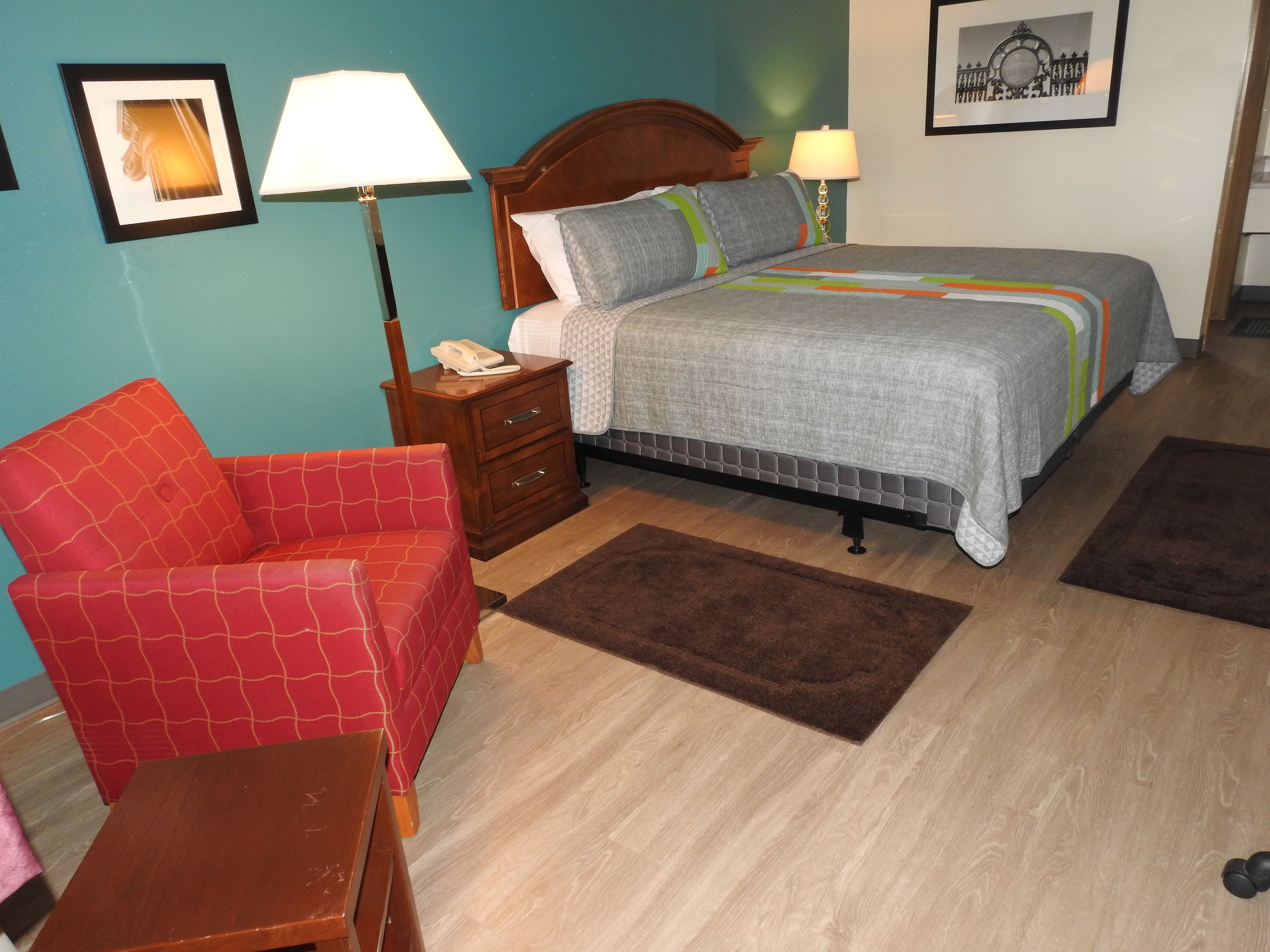 A bedroom with a bed, a nightstand, a red armchair, a wooden dresser, and a brown rug.