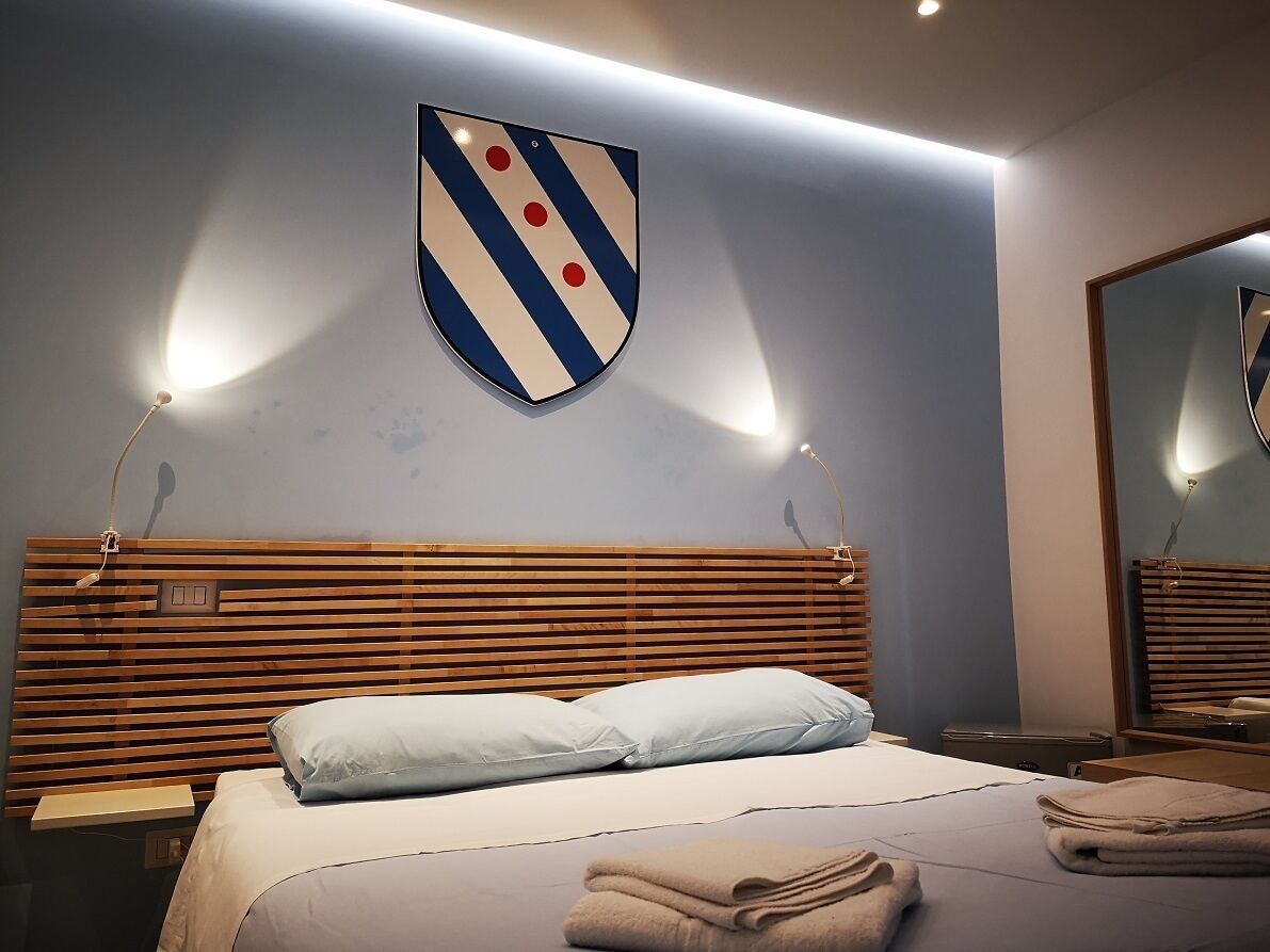 Ein Hotelzimmer mit einem hölzernen Kopfteil, einem Bett mit hellblauer Bettwäsche, einem auf dem Bett gefalteten Handtuch und einer schildförmigen Wanddekoration.