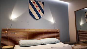Ein Hotelzimmer mit einem hölzernen Kopfteil, einem Bett mit hellblauer Bettwäsche, einem auf dem Bett gefalteten Handtuch und einer schildförmigen Wanddekoration.