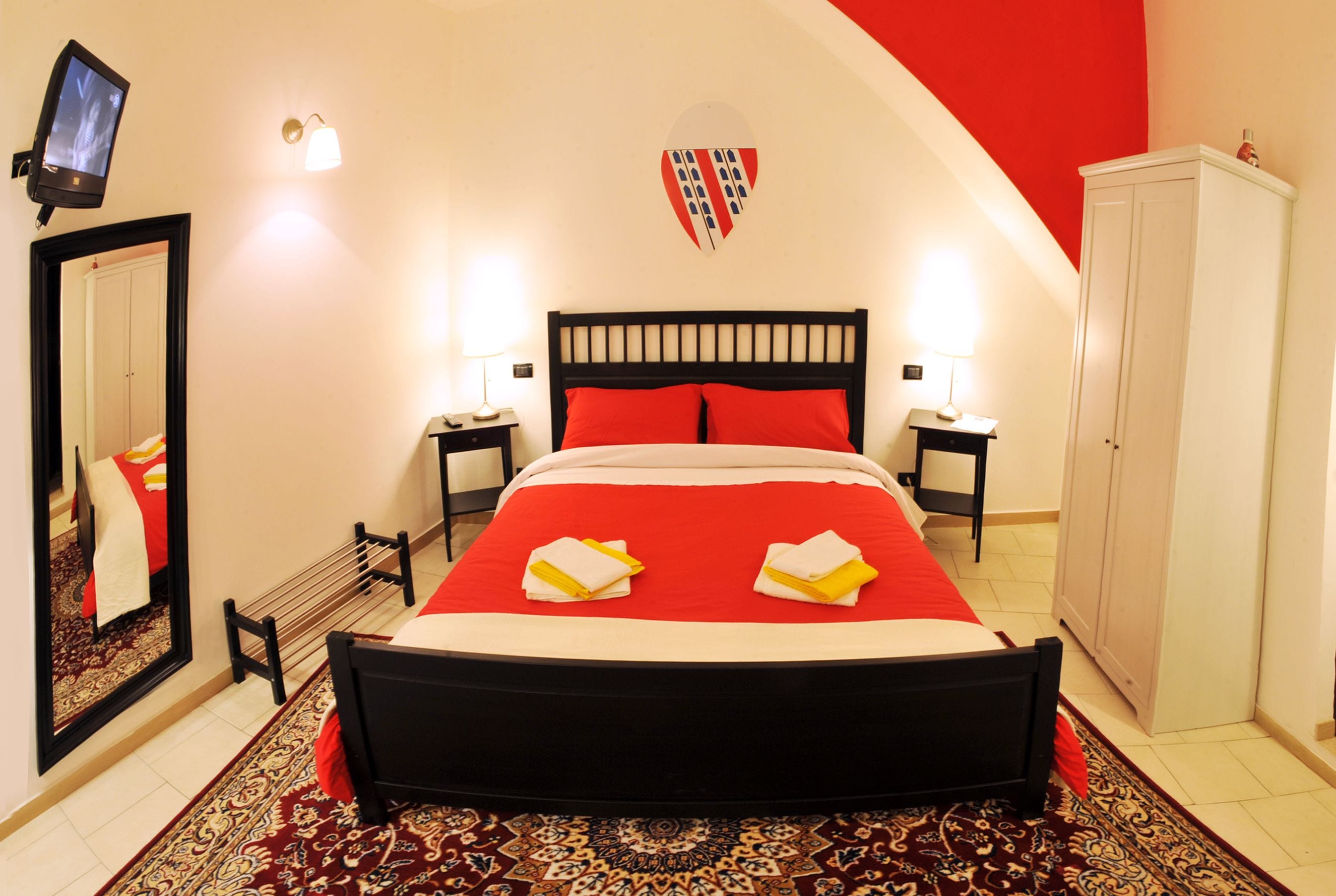 A hotel room with a large bed, two bedside tables, a mirror, a wardrobe, and a television on the wall.