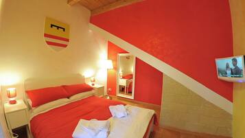 Une chambre d’hôtel aux couleurs rouge et blanc, avec un lit recouvert d’une literie rouge, une table de chevet avec une lampe, un miroir et un téléviseur fixé au mur.