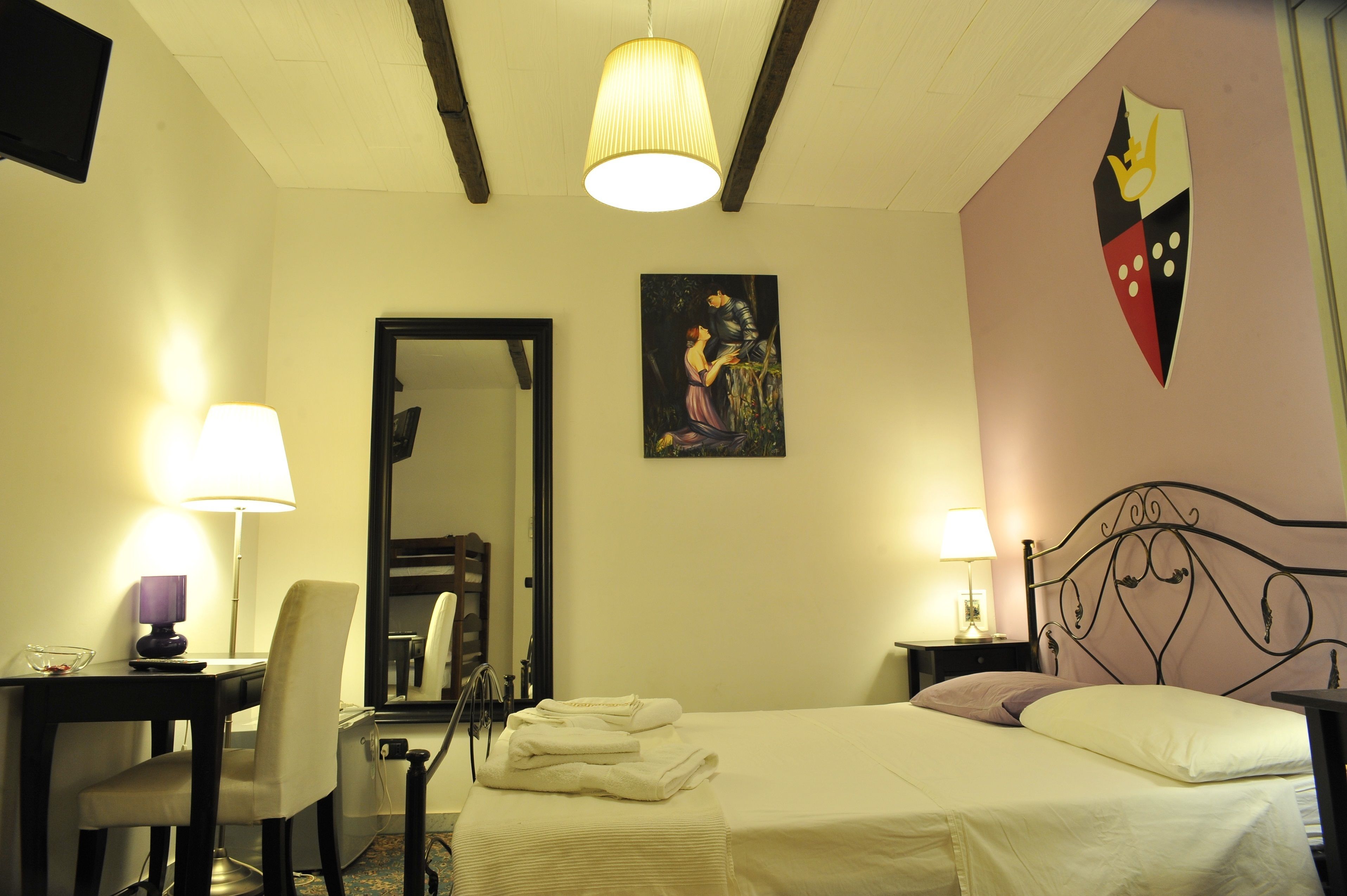 A hotel room with a bed, two bedside tables with lamps, a chair, a mirror, and a wall-mounted artwork.