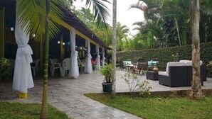 Un patio al aire libre con mesas y sillas, una zona cubierta con asientos y un pequeño jardín.