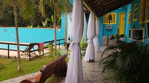 A poolside area with a blue pool, white curtains, and a yellow door. - Pousada Tropical Araçatiba (Angra dos Reis)