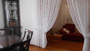 Ein Essbereich mit einem runden Tisch und Stühlen, einem Schrank mit Glastüren und einer Couch im Hintergrund.