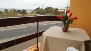 Ein Balkon mit Tisch, Stühlen und einer Vase mit roten Blumen. Im Hintergrund sind eine Straße und Gebäude zu sehen.