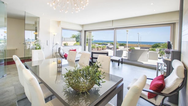 Un comedor moderno con una mesa de vidrio, sillas blancas y vista al mar.