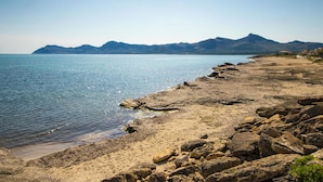 Una playa con costa rocosa, agua cristalina y montañas a lo lejos.