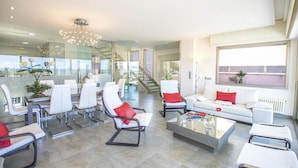 Una sala de estar moderna con un separador de vidrio, muebles blancos y una escalera que sube a un nivel superior.