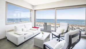 Un moderno salón con un sofá blanco, una mesa de centro y dos sillones, con vistas a una playa y al mar.