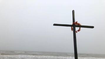 Une croix ornée d’une guirlande, placée sur un poteau au bord de la mer.