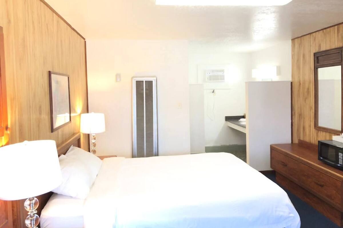 Habitación de hotel con cama, cómoda, espejo, lámpara y puerta que da a un baño.