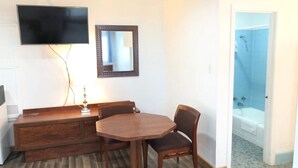 A hotel room with a wooden dining table, a TV mounted on the wall, a mirror, and a shower area visible through an open door. - Gulfway Motel & Restaurant (High Island)