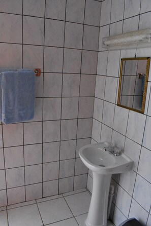 A bathroom with white tiled walls, a pedestal sink, a towel rack with a blue towel, and a mirror with a gold frame. - Aspid Apartments (Oranjestad)
